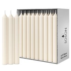 six white candles are lined up next to each other in front of a cardboard box