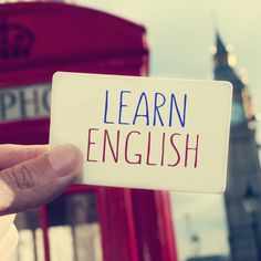 a hand holding up a sign that says learn english in front of a red phone booth