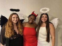 three women dressed up in devil costumes posing for a photo with one woman wearing an angel costume