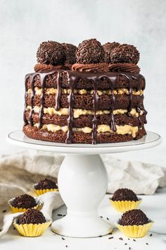 a cake with chocolate frosting and mini cupcakes next to it on a white pedestal