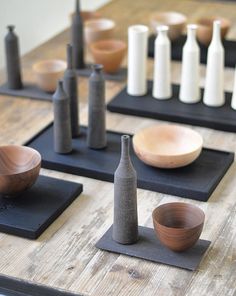 several different types of bowls and vases on black trays with wooden spoons