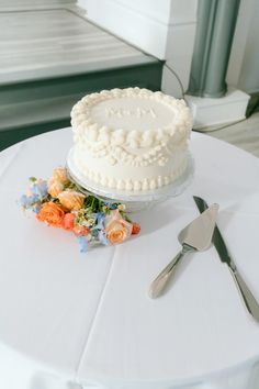 a white cake sitting on top of a table next to a knife and flower arrangement