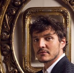 a man in a suit and tie looking at the camera with a gold framed mirror behind him