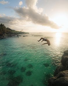 a man diving into the ocean from rocks in front of an island with green water