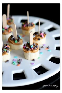 banana peanut butter bites with sprinkles are on a white plate and have toothpicks sticking out of them