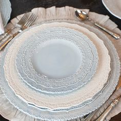 white plates and silverware are arranged on a wooden table with lace trimmings