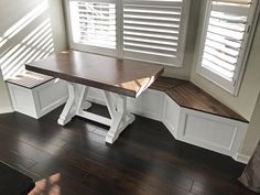 a wooden table and bench in a room with white shutters on the window sill