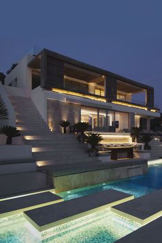 a large modern house with stairs leading up to the upper level and pool area at night