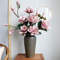 a vase filled with pink flowers sitting on top of a wooden table next to a mirror