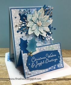 a blue and white christmas card with snowflakes, holly leaves and poinsettis