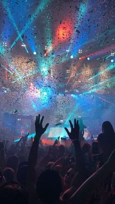 people at a concert with confetti falling from the ceiling and hands in the air