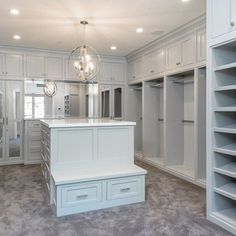 a large walk in closet with white cabinets and drawers on the walls, along with a chandelier hanging from the ceiling