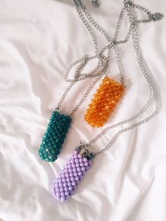 three beaded necklaces sitting on top of a white bed next to each other