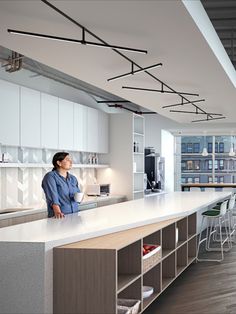 a woman standing at the counter in a large kitchen with lots of white cupboards