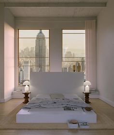 a large bed sitting in the middle of a room next to two windows with city lights on them