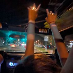 two people in a car with their hands up and the lights on at night behind them