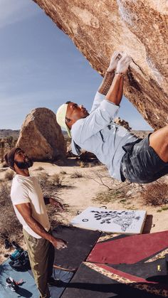 a man on a rock climbing up the side of a mountain while another man watches