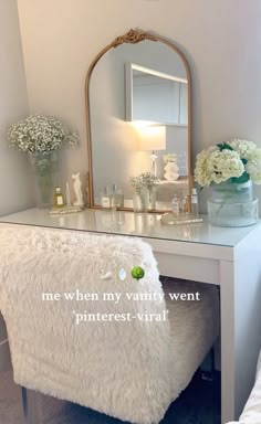 a vanity with a mirror, vases and flowers on the top shelf next to it