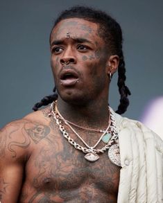 a shirtless man with tattoos on his chest wearing a white jacket and chain around his neck