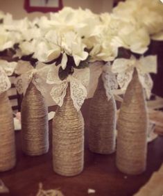 several vases with white flowers in them on a wooden table and some burlocks