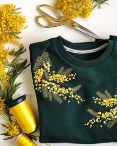 a green sweater with yellow flowers on it next to a pair of scissors and some plants