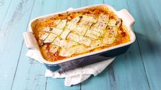 a casserole dish with zucchini and cheese in it on a blue wooden table