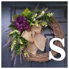 a wreath with the letter s on it and flowers hanging from it's front door