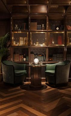 two green chairs sitting in front of a wooden book shelf filled with lots of books