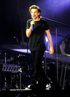 a male in a black shirt is standing on stage and holding a microphone to his mouth