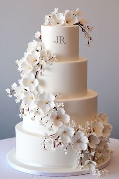 a three tiered wedding cake with white flowers on the top and initials on the side