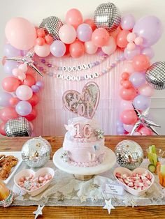 a table topped with a cake and lots of balloons