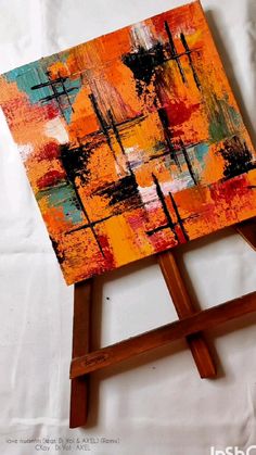 an orange and black abstract painting on a wooden easel