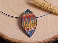 a wooden necklace with a colorful design on it's end and a wheat stalk in the background