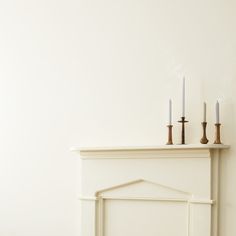 a fireplace with three candles on top of it next to a white wall and floor