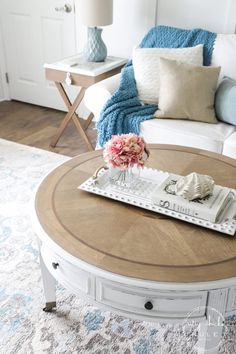 a coffee table with flowers on it in front of a white couch and blue throw pillows