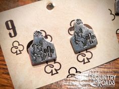 two metal earrings sitting on top of a wooden table next to numbers and symbols in the shape of hearts