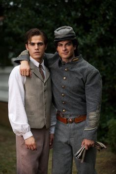 two men dressed in period clothing standing next to each other with trees in the background