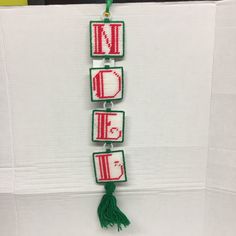 a cross stitch name sign hanging from a wall with tassels attached to it