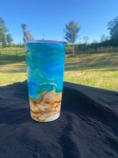 a blue and yellow cup sitting on top of a black tablecloth in the middle of a field