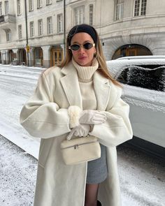 a woman standing in the snow with her hand on her hip, wearing a white coat and black hat