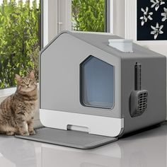 a cat sitting on the floor next to a gray and white house shaped litter box