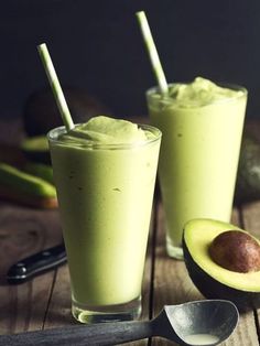 two glasses filled with green smoothie next to an avocado