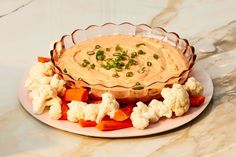 a plate topped with cauliflower and carrots next to a bowl of dip