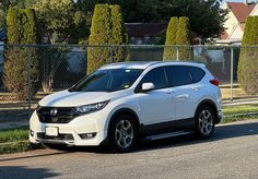 a white honda cr - v is parked on the side of the road in front of a fence