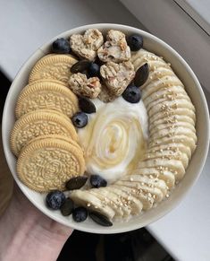 a white bowl filled with cookies, blueberries and other food items next to a window