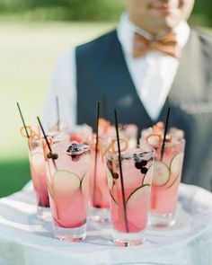 a man in a bow tie holding a tray with glasses filled with drinks on it