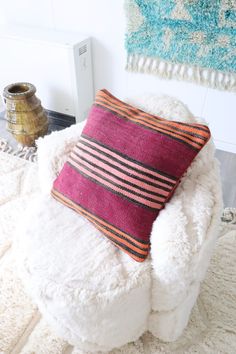 a white chair with a pink and orange pillow on it next to a blue rug