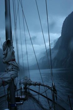 the back end of a sailboat on a body of water with mountains in the background