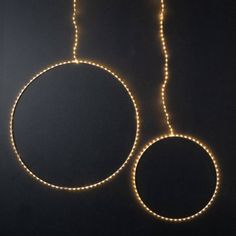 two circular lights are hanging from the ceiling in front of a black wall and floor