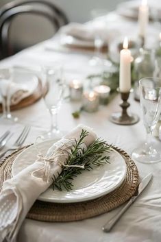 Thanksgiving Table Setting Ideas for Small Spaces - Nordic Simplicity. Linen table cloth, rustic woven chargers, white ceramic plates, white candles and a simple centerpiece consisting of seasonal foliage. And an elegantly folded linen napkin tied with a rustic thread and a stem of eucalyptus leaves. White And Ivory Table Setting, Holiday Plates Table Settings, White Tablecloth Thanksgiving Table, Tablecloth Setting Ideas, White Christmas Dinner Party, Table Decor For Thanksgiving Dinner, Christmas Table For Two, White Table Setting Christmas